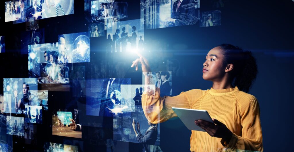 Frau im gelben Pullover mit Tablet berührt eine Wand aus leuchtenden Bildschirmen - Insight zu Omnichannel mit Content und Commerce