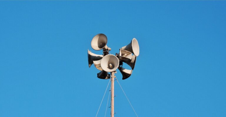 Gruppe von Lautsprecher-Megafonen auf einem Mast vor blauem Himmel - Erfolgs-Projekt im Handel bei mpcg