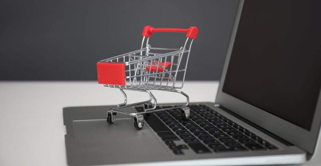 Kleiner roter Miniatur-Einkaufswagen steht auf einer Laptop-Tastatur - Insight zum E-Commerce