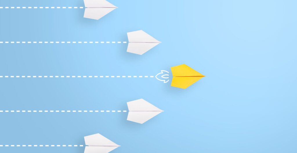 Gelbes Papierflugzeug führt eine Gruppe weißer Papierflugzeuge auf hellblauem Hintergrund an - Insight zu Leadership im digitalen Zeitalter