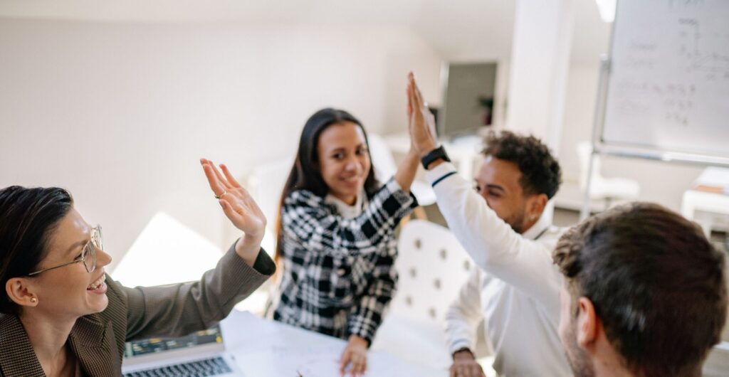 Vier lächelnde Kollegen geben sich am Besprechungstisch High-Five - Erfolgs-Projekt im Gesundheitswesen