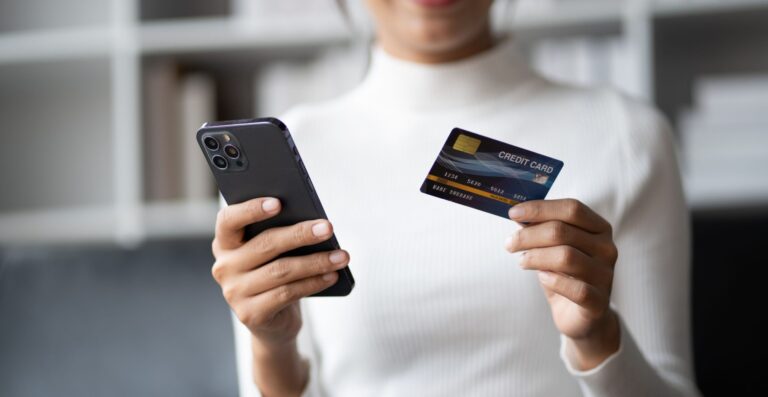Person im weißen Pullover hält Smartphone und Kreditkarte in den Händen - Erfolgs-Projekt im Handel bei mpcg
