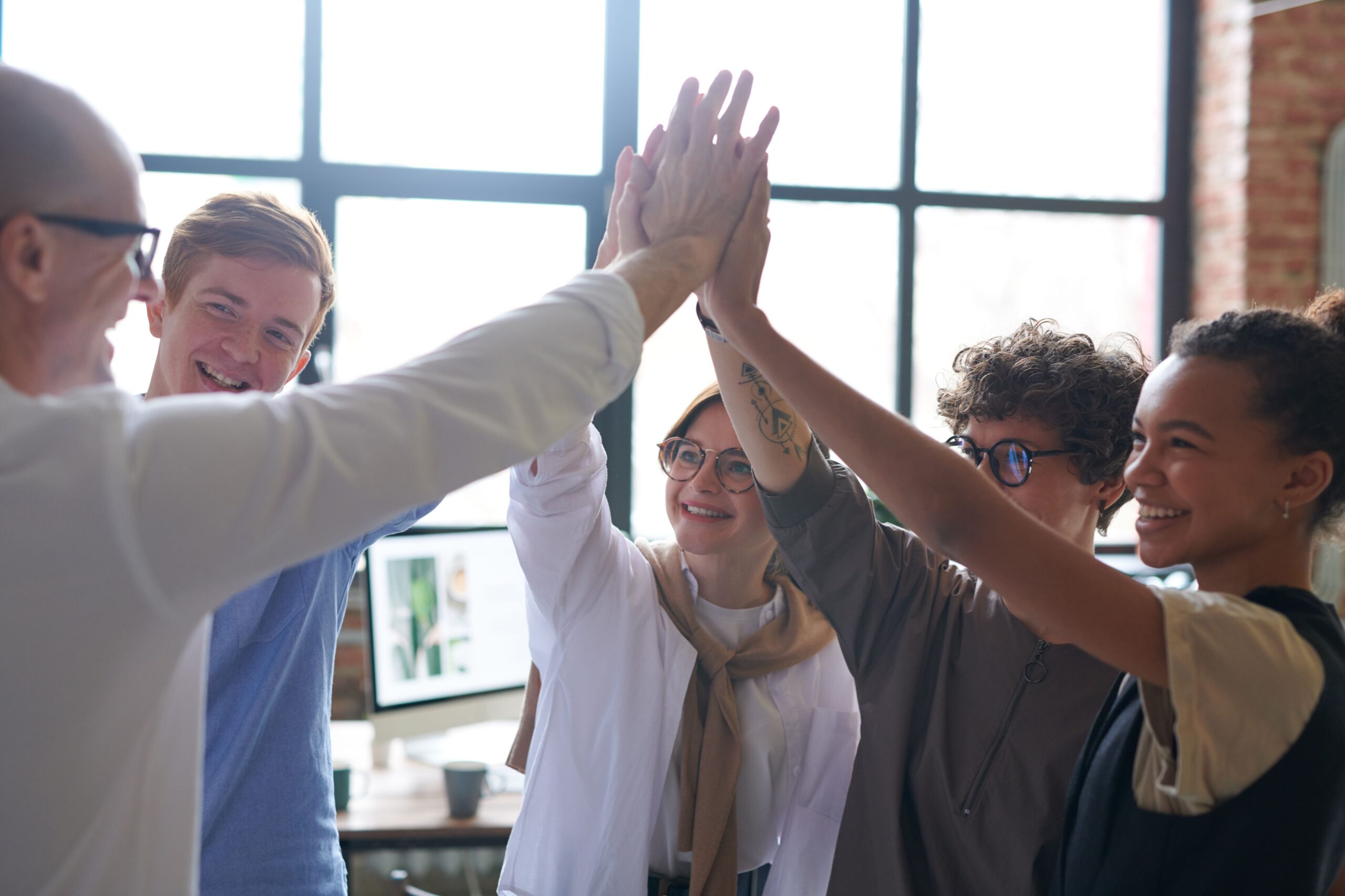 Fünf Kolleginnen und Kollegen beim High-Five im Büro - Teamkultur bei der mpcg